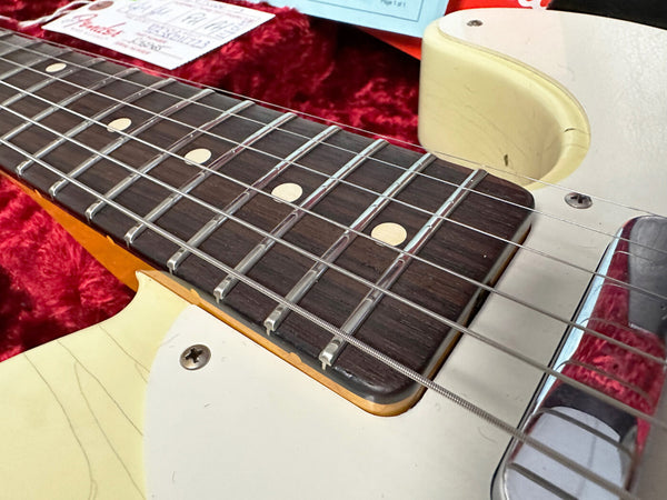 Close-up of electric guitar fretboard and strings on white body with red plush case background, vintage-style maple neck and chrome bridge plate