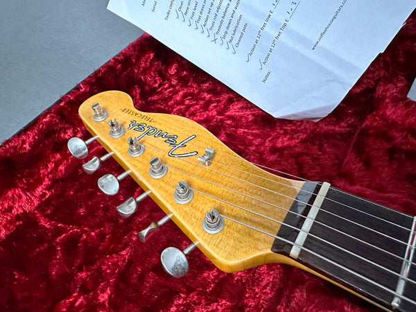 Close-up of Fender Telecaster guitar headstock on red plush case lining with maintenance checklist paper