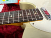 Close-up of cream electric guitar neck, rosewood fretboard with dot inlays, and chrome pickup on red velvet background