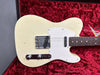 Vintage cream electric guitar body with white pickguard and metal bridge, resting on red plush interior of custom guitar case