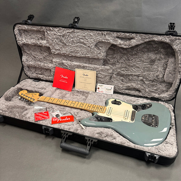Fender electric guitar in seafoam green finish with maple neck, displayed in an open hard guitar case with plush gray interior, accompanied by Fender authenticity certificate, tags, and accessories.