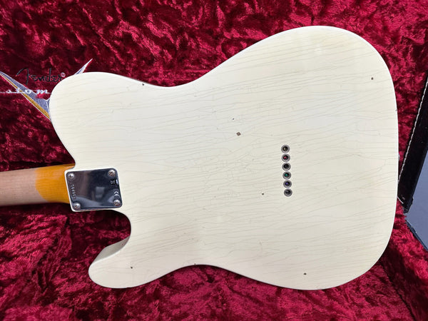 White electric guitar body with vintage crackle finish and string ferrules, resting on red plush Fender guitar case lining