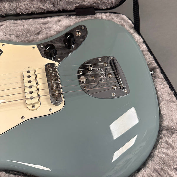 Close-up of seafoam green electric guitar body with chrome bridge and black control knobs in a gray plush guitar case interior