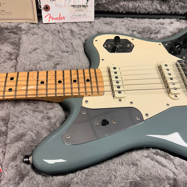 Close-up of a Fender electric guitar body and maple fretboard with single-coil pickups, chrome hardware, and gray finish on a soft gray surface.