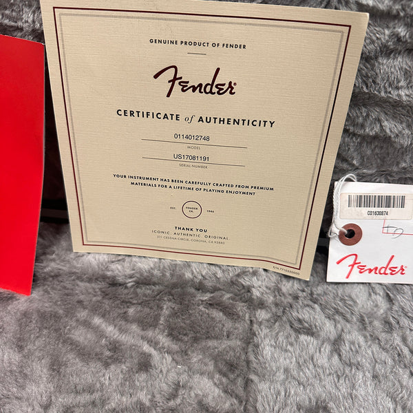 Fender certificate of authenticity with model and serial number on gray fabric background next to Fender tag and red booklet