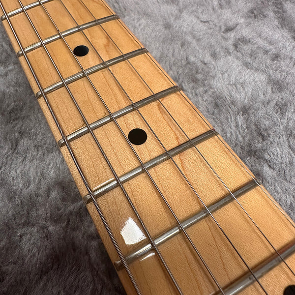 Close-up of maple guitar neck fretboard with metal frets and black dot inlays on grey plush background