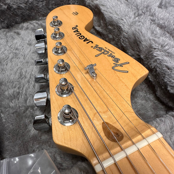Close-up of Fender Jaguar guitar headstock with chrome tuning pegs on soft gray guitar case interior