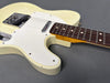 Close-up of vintage cream-colored electric guitar body and rosewood fretboard on gray background