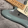 Close-up of electric guitar body with metallic blue finish, maple fretboard, and chrome control plate on gray plush surface