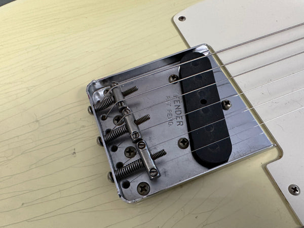 Close-up of Fender Telecaster vintage-style bridge with saddles and single-coil pickup on cream electric guitar body