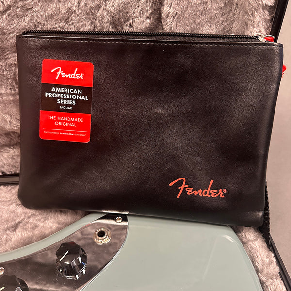 Fender American Professional Series Jaguar guitar accessory pouch with black leather texture and red Fender logo placed on light blue electric guitar in padded case