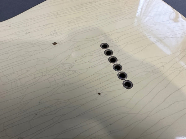 Close-up of light-colored guitar body showing fine cracks and two small chips around string ferrules holes