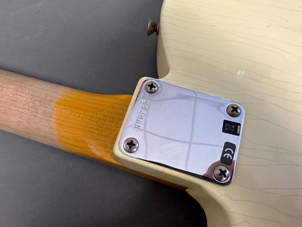 Close-up of guitar neck joint with metal neck plate and screws on cream-colored electric guitar with natural wood neck and vintage wear