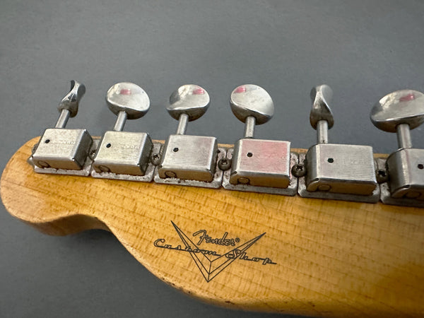 Close-up of vintage Fender Custom Shop guitar headstock showing six tuning pegs on light wood grain with black Fender Custom Shop logo.
