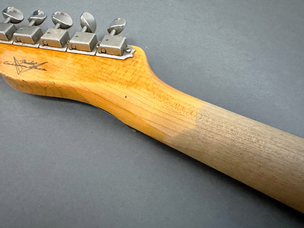 Close-up of worn Fender guitar maple neck and vintage tuning machines against a gray background