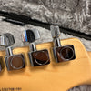 Close-up of Fender guitar tuning pegs on natural wood headstock against plush grey fabric background