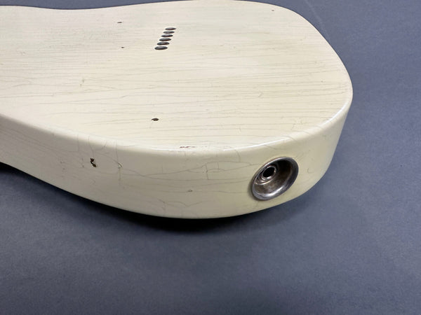 Close-up of vintage cream electric guitar body showing input jack and textured finish with cracks and wear