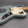 Close-up of light blue electric guitar body with white pickguard, two single-coil pickups, black control knobs, and light maple neck on gray background