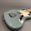 Close-up of light blue electric guitar body with maple neck, chrome bridge, black control knobs, and off-white pickguard on gray background