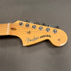 Close-up of natural wood Fender Jaguar guitar headstock with chrome tuning pegs and black logo text on gray background