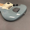 Close-up of a light blue electric guitar body with cream pickguard, black control knobs, and chrome bridge and tailpiece on a gray surface.