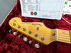 Close-up of Fender Stratocaster guitar headstock with vintage tuning pegs on red velvet case lining and partial certificate sheet in background