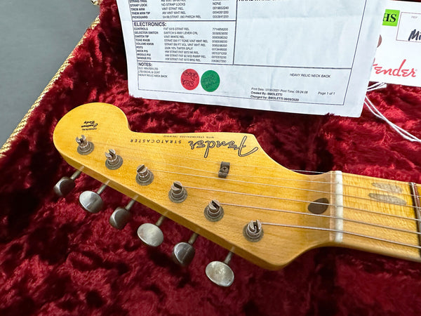 Close-up of Fender Stratocaster guitar headstock with vintage tuning pegs on red velvet case lining and partial certificate sheet in background