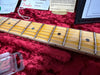 Close-up of vintage Fender guitar maple neck and fretboard with wear marks, silver frets, and dot inlays on red plush case lining with Fender tags and paperwork