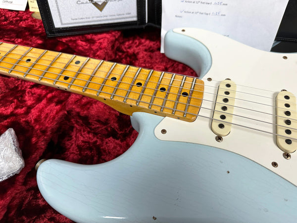 Close-up of light blue electric guitar body with vintage maple neck and white pickups on red plush guitar case lining