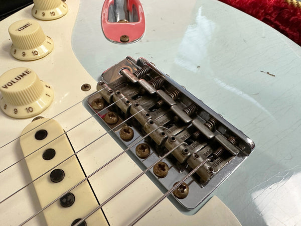 Close-up of vintage electric guitar bridge, six strings, volume and tone control knobs with creamy aging on a light blue body showing wear and scratches