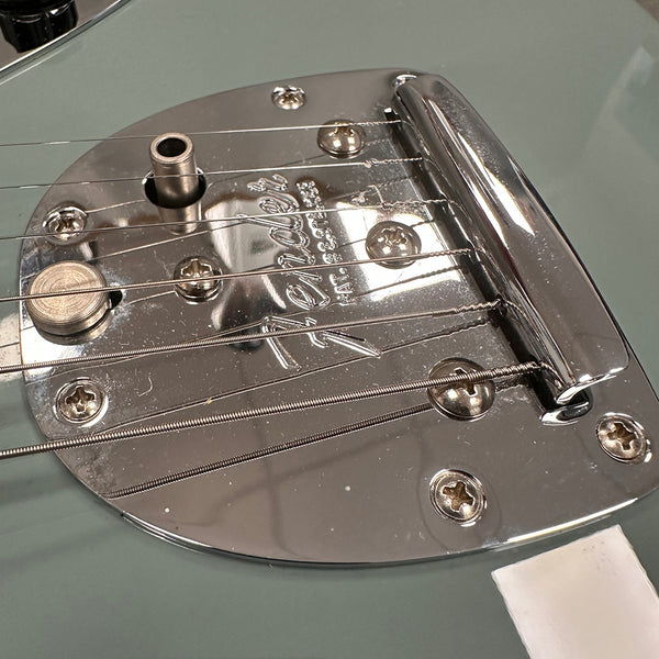 Close-up of Fender guitar chrome bridge and tailpiece with strings on light blue electric guitar body