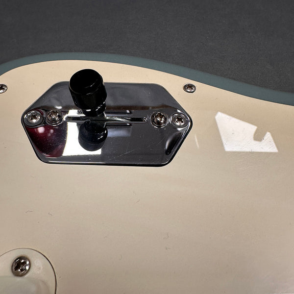 Close-up of a white electric guitar body showing a chrome pickup selector switch plate and black toggle switch knob with screws and light reflections.