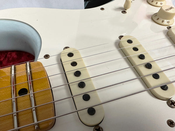 Close-up of white electric guitar pickups and strings with cream-colored volume knobs and a wooden fretboard edge in Guitar case with red lining, Coffee House Guitars product image