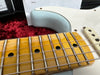Close-up view of vintage maple fretboard and strings on light blue electric guitar body with white pickguard and pickups on red plush background