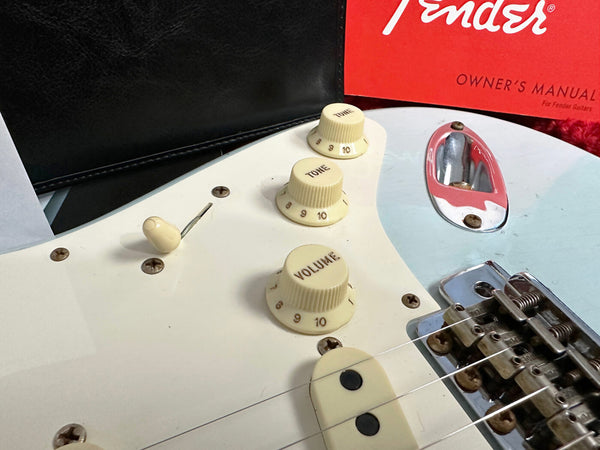 Close-up of white Fender Stratocaster electric guitar control knobs including volume and tone with Fender owner's manual in background
