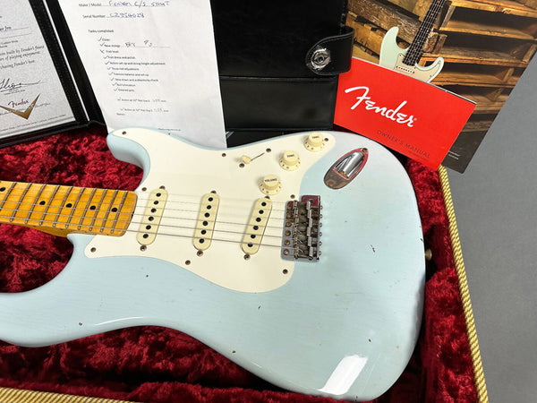 Fender Custom Shop Stratocaster electric guitar in light blue with maple neck resting in red plush-lined case, accompanied by Fender certificate, setup checklist, leather case folder, and Fender owner's manual.