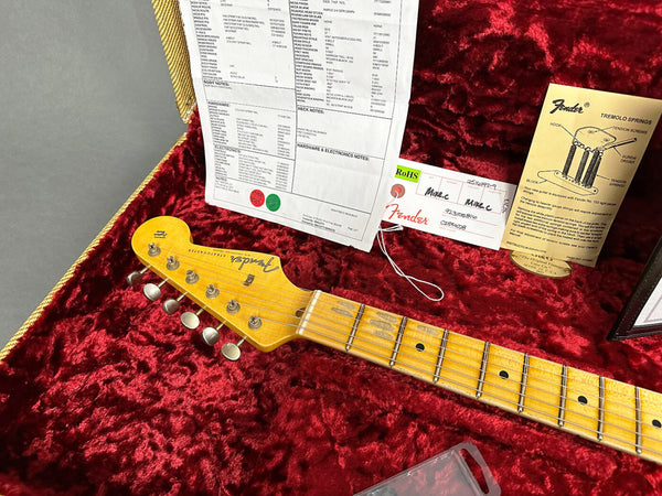Close-up of Fender Stratocaster guitar neck and headstock in red velvet case with Fender certification papers and tremolo springs instruction booklet.