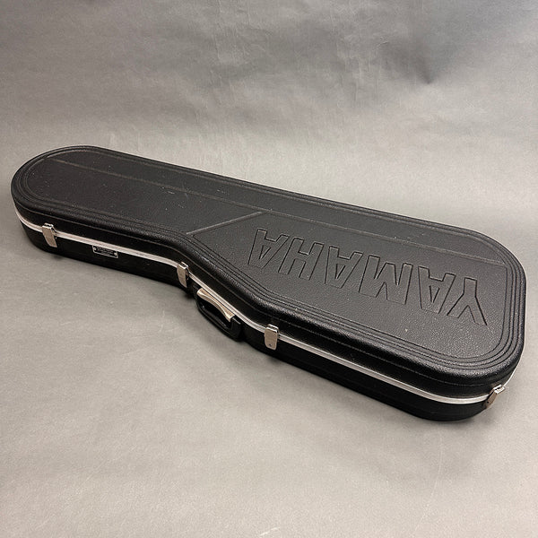 Black Yamaha hard shell guitar case with silver latches and handle on gray background