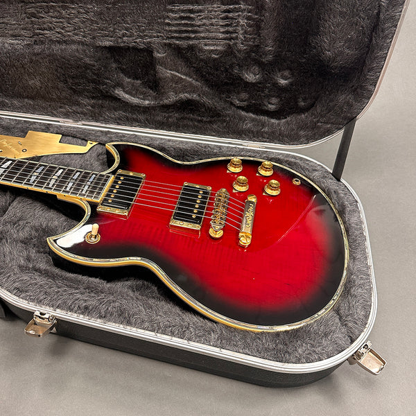 Electric guitar with sunburst finish, gold hardware, and humbucker pickups in a gray plush-lined hard case