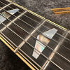 Close-up of guitar fretboard with mother-of-pearl trapezoid inlays and steel strings on dark wood fingerboard