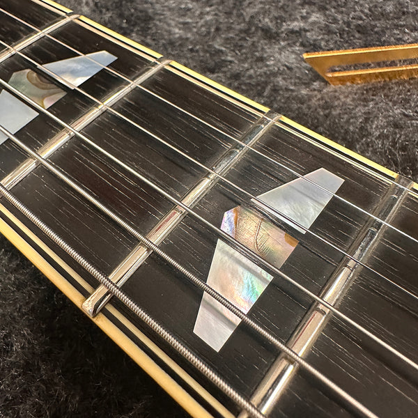 Close-up of guitar fretboard with mother-of-pearl trapezoid inlays and steel strings on dark wood fingerboard