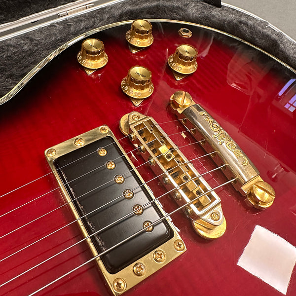 Close-up of red electric guitar body showing gold tone knobs, black pickup with gold screws, and detailed gold bridge and tailpiece