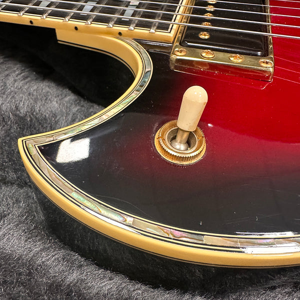 Close-up of electric guitar toggle switch with cream-colored tip on red and black sunburst body featuring mother of pearl and cream binding detail
