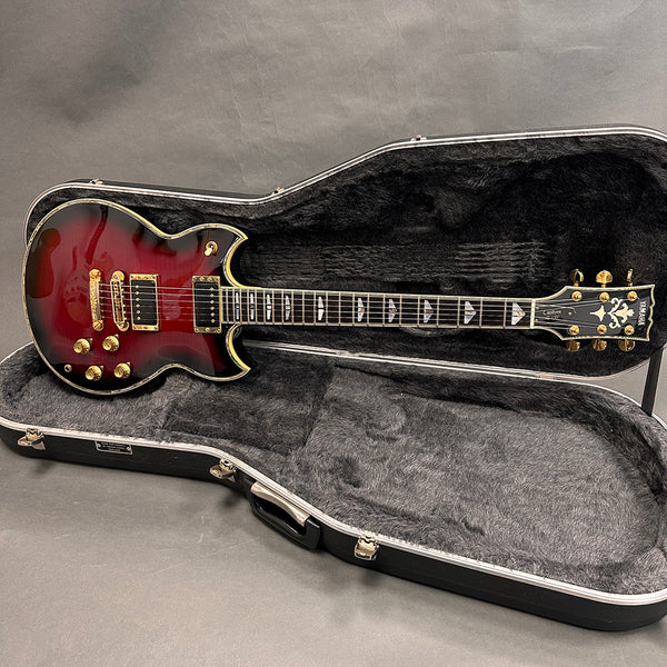 Yamaha electric guitar with deep red sunburst finish, gold hardware, and unique triangular inlays, displayed inside black plush-lined hardshell case on gray background.