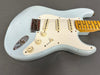 Light blue electric guitar with maple fretboard, three single-coil pickups, white pickguard, two tone knobs, one volume knob, and chrome bridge on gray surface