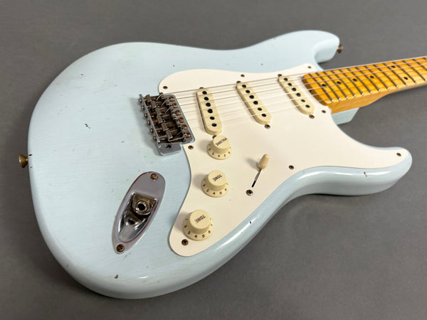 Light blue electric guitar with white pickguard, three single-coil pickups, volume and tone control knobs, maple neck, and chrome hardware on gray background