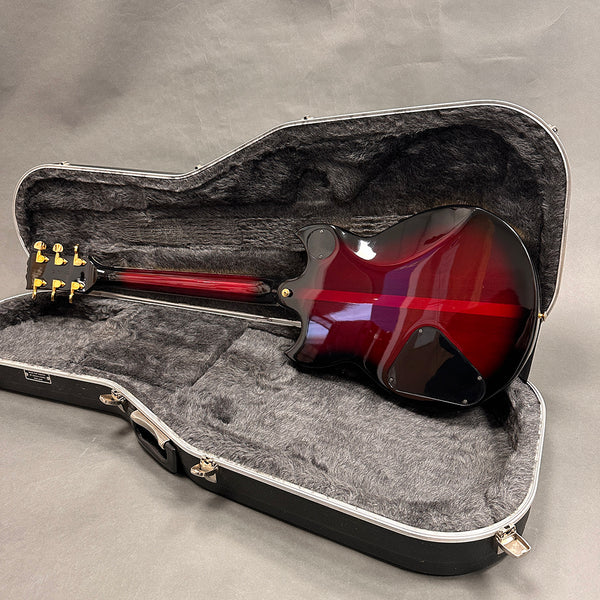 Electric guitar with red sunburst finish and gold tuning pegs displayed inside gray plush-lined black hard case