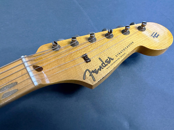 Close-up of Fender Stratocaster guitar headstock with six tuning pegs on blue background