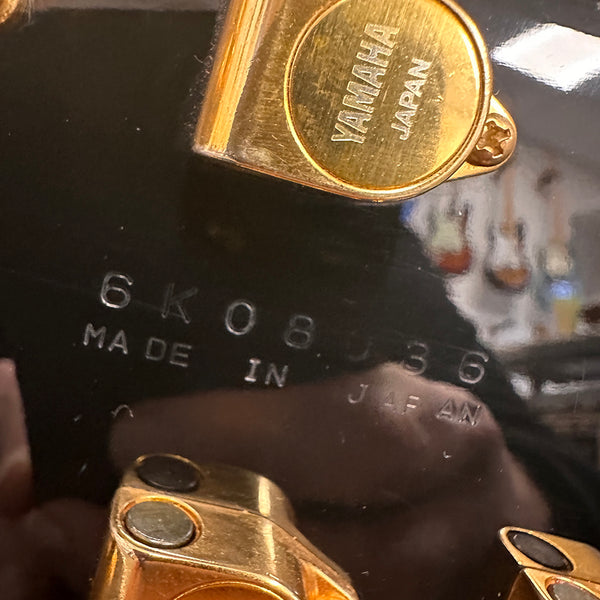 Close-up of gold Yamaha tuning peg and serial number 6K0836 on black guitar headstock, made in Japan guitar part detail