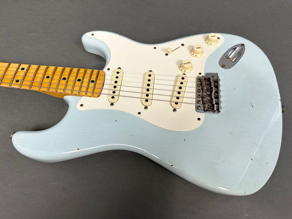 Light blue vintage electric guitar with maple neck, white pickguard, and three single-coil pickups on gray background